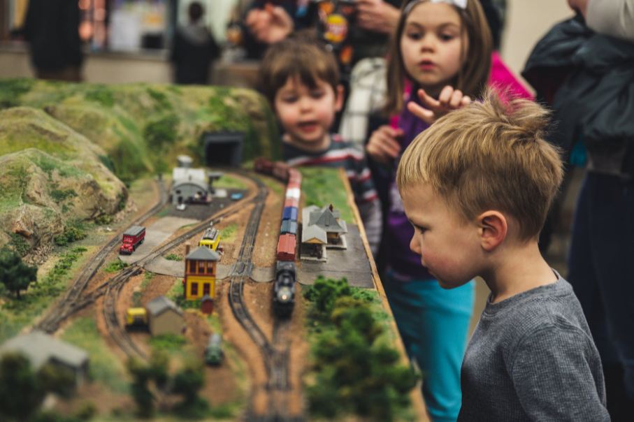 boy-standing-near-miniature-train-toys