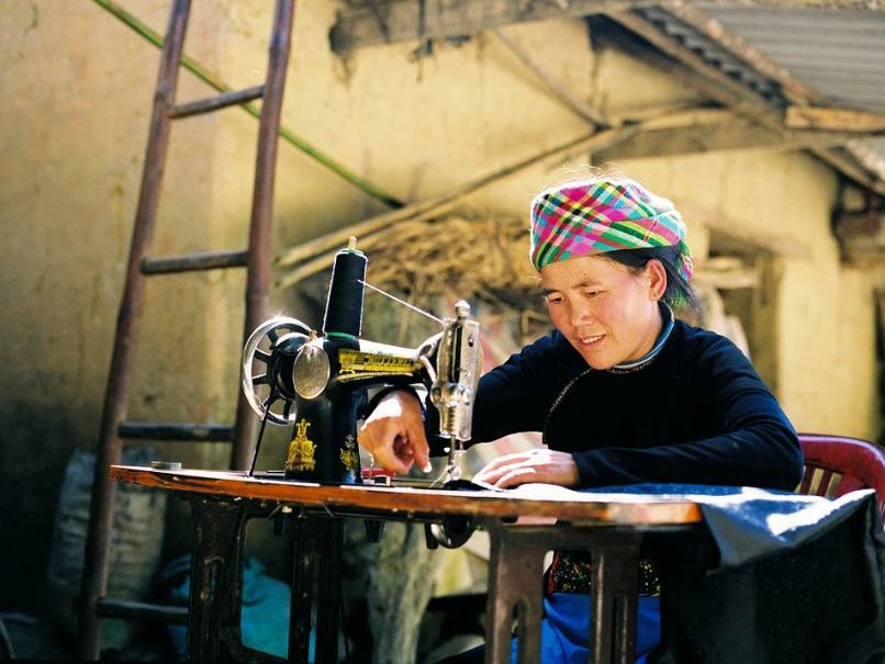 a woman sewing, a woman with colourful headdress, a woman wearing black, sewing machine
