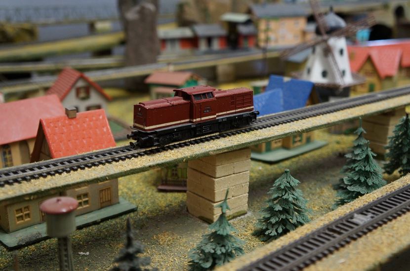 railway, a red train on the railway, pine trees, houses, toy
