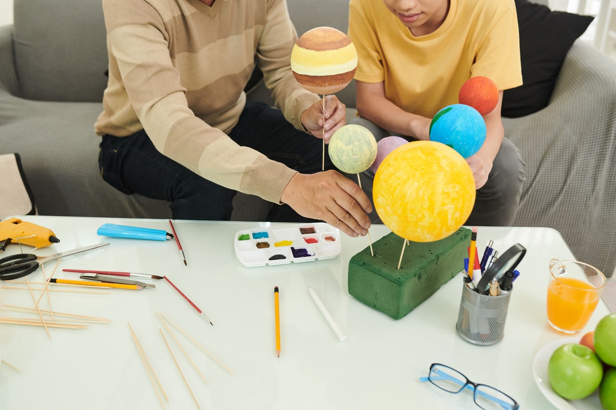 Father and son putting spikes into styrofoam planets when painting it for Solar System project