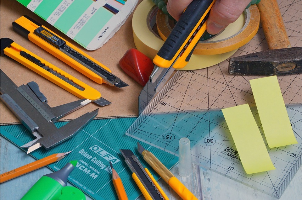 different types of cutters, rulers, and adhesive on top of a cutting mat