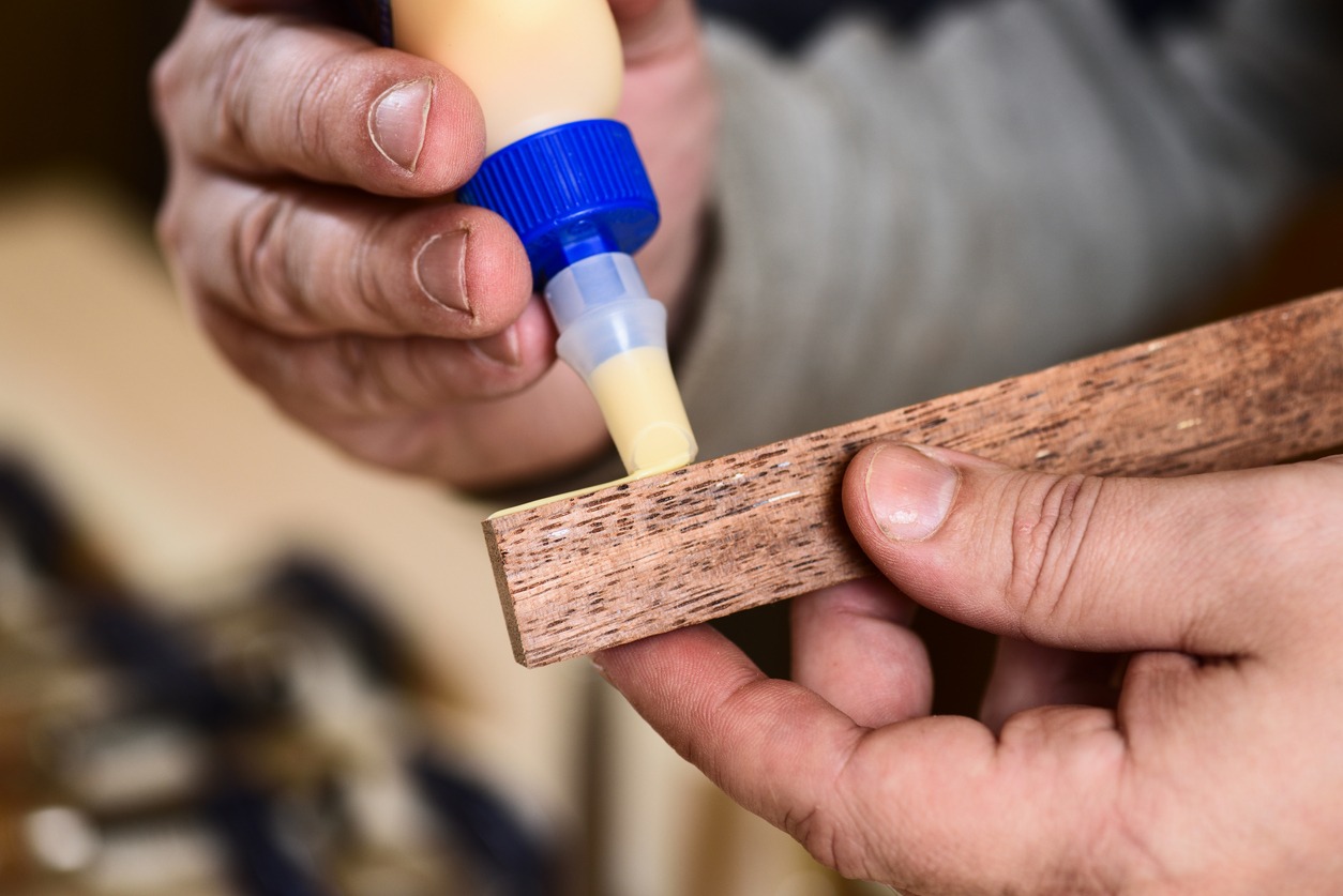 a man holding a bottle of wood glue and applying it on a block of wood
