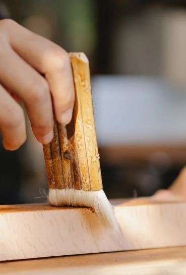 a close up of a person’s hand brushing liquid on a piece of wood