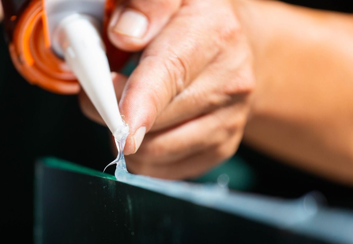 a hand gluing silicone on the edge of the glass