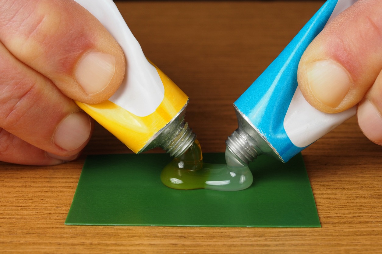 a hand holding two tubes with epoxy glue ingredients: resin and hardener