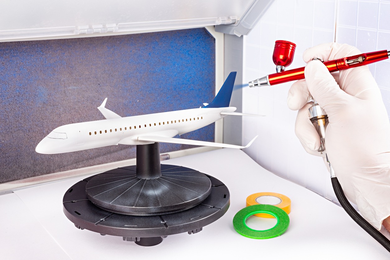 Paint job with red metal airbrush spray paint gun on red scale model modern white blue passenger airplane