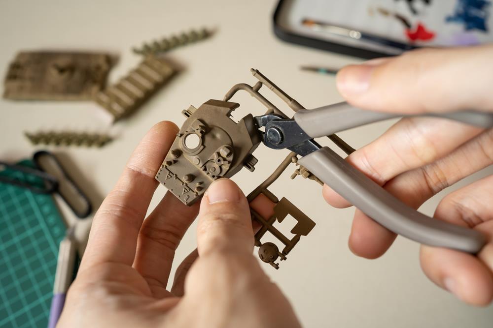Close-up of hands using precision cutters to trim plastic parts from a model kit fram