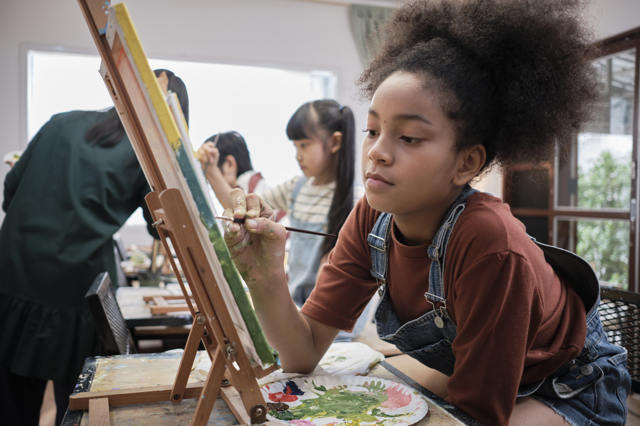 A girl concentrates on acrylic color painting on canvas in an art classroom